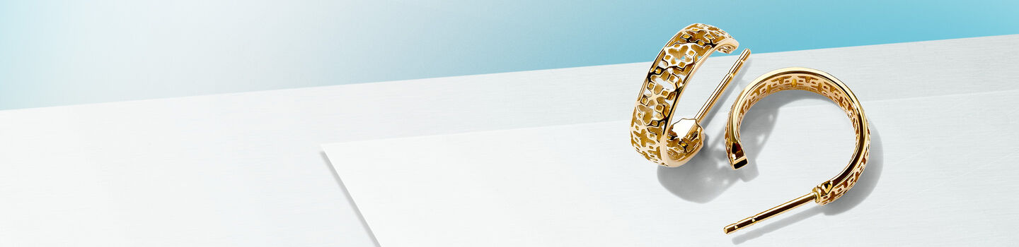 Birks Muse gold hoop earrings on a blue background.